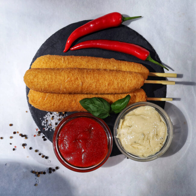 Corn dogs with sauces and red chili peppers on a black plate